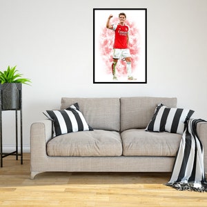 May include: A framed watercolor painting of a soccer player in a red and white jersey with the text "Emirates Fly Better" on the front. The player is raising his right arm in celebration. The background is a pink and white watercolor wash.