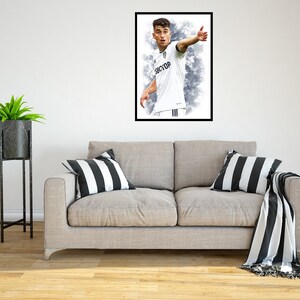 May include: A framed photograph of a football player wearing a white kit with black accents. The player is wearing black shorts and white socks. The player is looking to the right and has his right arm extended. The jersey has the text "38CYOP" on the front.