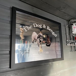 Może przedstawiać: Czarne lustro w ramie z białym napisem "The Dog & Bengal Est. 2020". Lustro odbija bar z kranami i figurką psa.