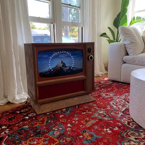 May include: A vintage-style television with a wooden cabinet and a red panel. The screen displays the Paramount Pictures logo. The TV sits on a patterned red rug in a living room setting.