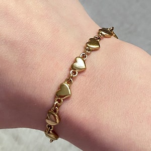 K&ouml;nnte beinhalten: Ein goldenes Armband mit einer Kette aus kleinen herzf&ouml;rmigen Gliedern.