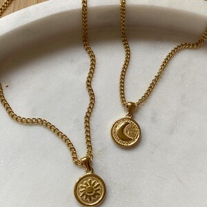 May include: Two gold chain necklaces with pendants. One pendant is a sun with a textured surface and the other is a crescent moon with a textured surface.