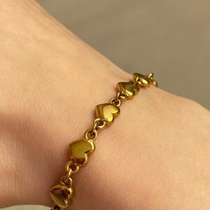 K&ouml;nnte beinhalten: Ein goldenes Armband mit herzf&ouml;rmigen Gliedern. Das Armband besteht aus einer Reihe von miteinander verbundenen herzf&ouml;rmigen Gliedern.