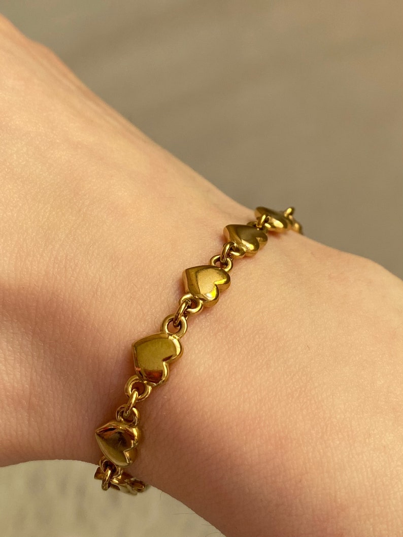 K&ouml;nnte beinhalten: Ein goldenes Armband mit herzf&ouml;rmigen Gliedern. Das Armband besteht aus einer Reihe von miteinander verbundenen herzf&ouml;rmigen Gliedern.