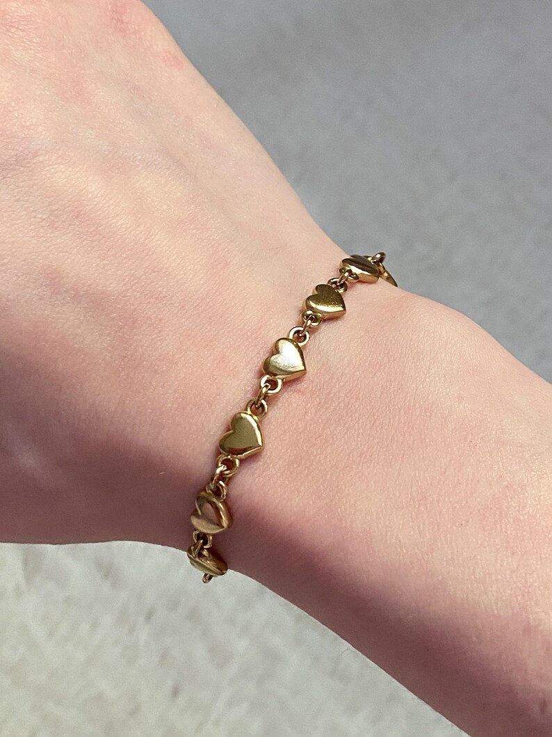 K&ouml;nnte beinhalten: Ein goldenes Armband mit einer Kette aus kleinen herzf&ouml;rmigen Gliedern.