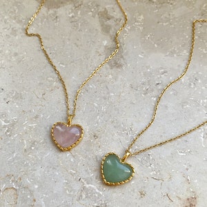 May include: Two gold necklaces with heart-shaped pendants. One pendant is a light pink heart, the other is a light green heart.