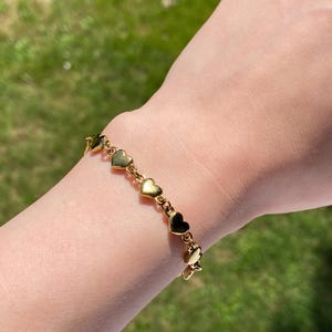 K&ouml;nnte beinhalten: Ein goldenes Armband mit einer Kette aus kleinen Herzanh&auml;ngern.