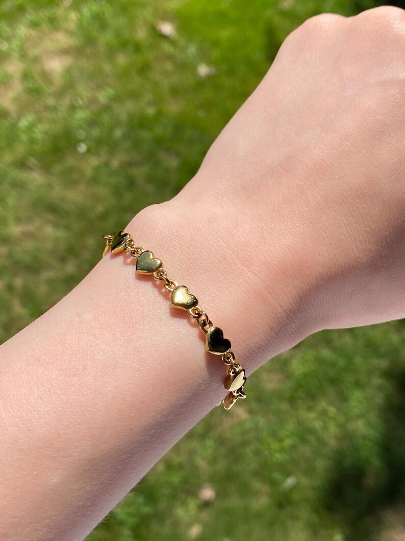 K&ouml;nnte beinhalten: Ein goldenes Armband mit einer Kette aus kleinen Herzanh&auml;ngern.