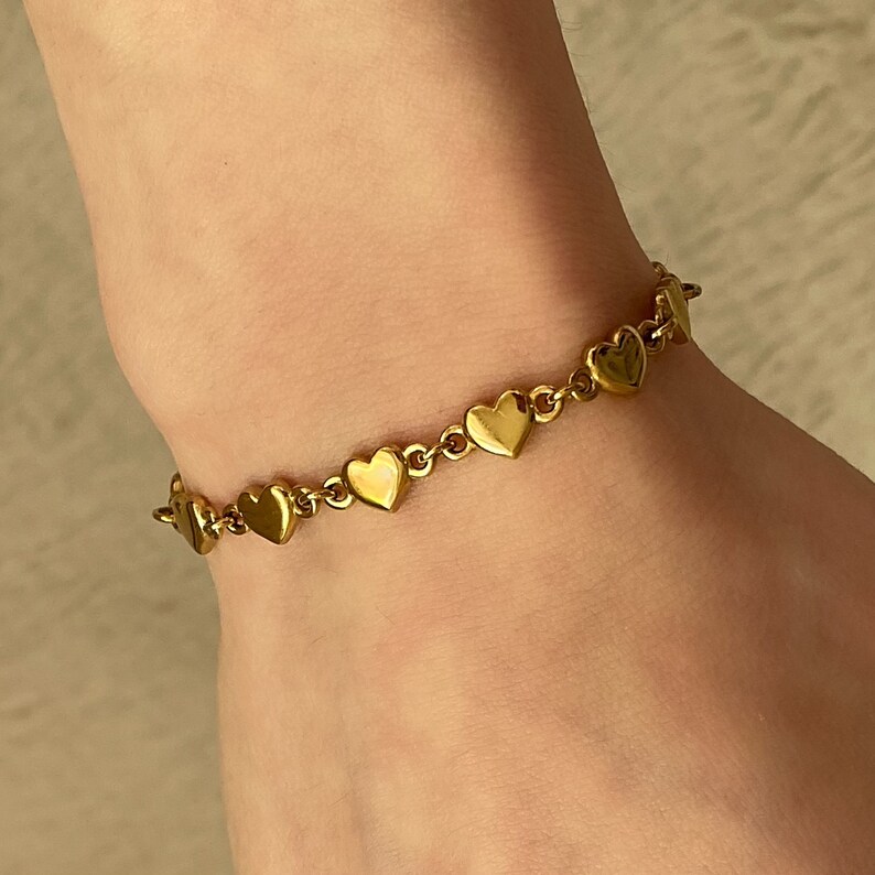K&ouml;nnte beinhalten: Ein goldenes Armband mit Herz-Anh&auml;ngern. Das Armband hat eine zarte Kette und kleine, herzf&ouml;rmige Anh&auml;nger.