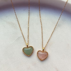 May include: Two gold necklaces with heart-shaped pendants. One pendant is a light green stone and the other is a light pink stone.
