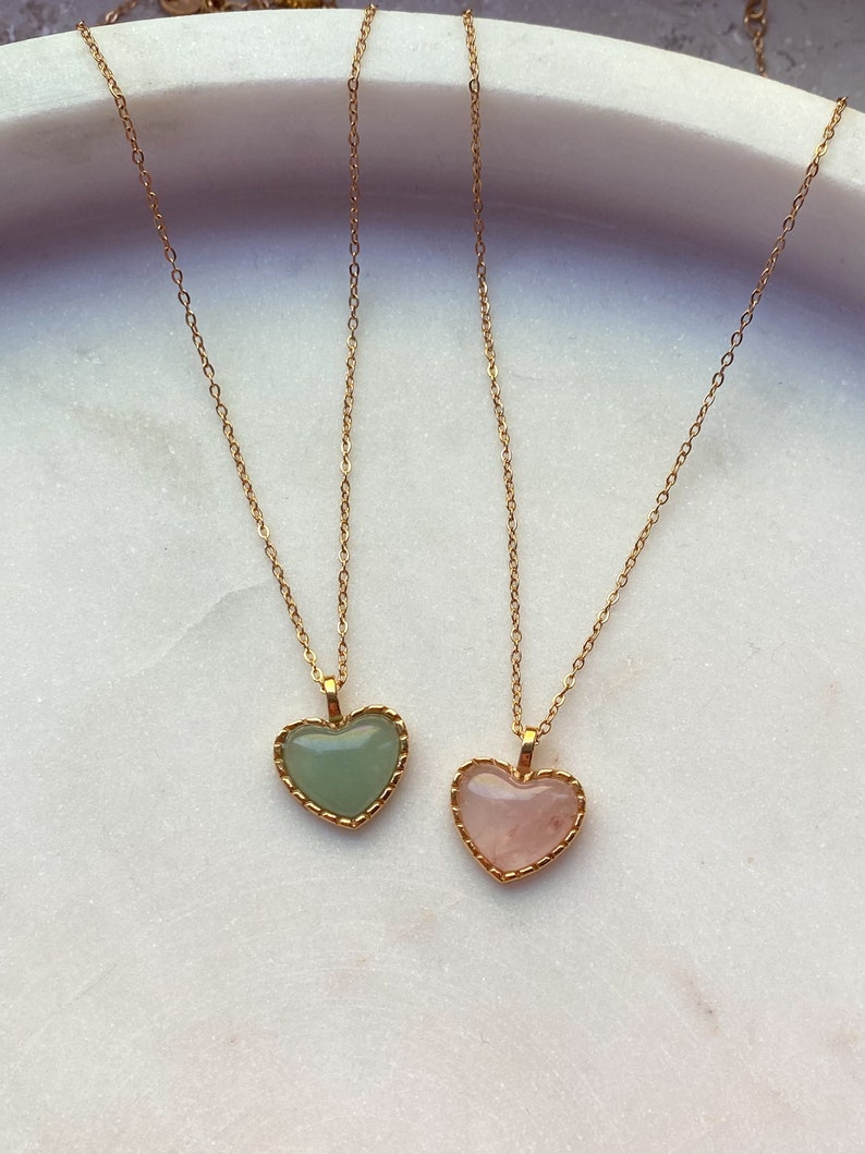 May include: Two gold necklaces with heart-shaped pendants. One pendant is a light green stone and the other is a light pink stone.