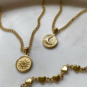 May include: Three gold necklaces with different pendants. One necklace has a sun pendant, another has a moon pendant, and the third has a chain of small hearts.