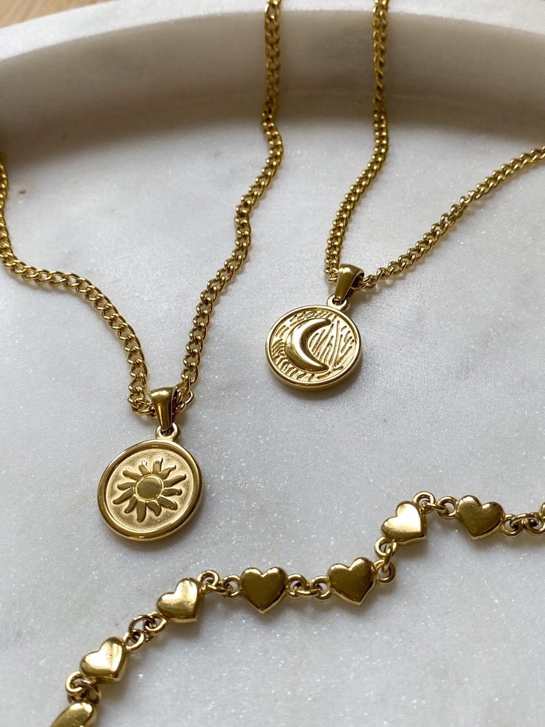 May include: Three gold necklaces with different pendants. One necklace has a sun pendant, another has a moon pendant, and the third has a chain of small hearts.