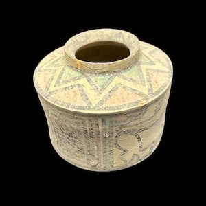 May include: A small, cylindrical ceramic vessel with a matte, light beige finish. The top shoulder features a repeating star pattern in muted green and salmon pink, outlined in dark gray. The sides display vertical lines and abstract dark gray motifs.