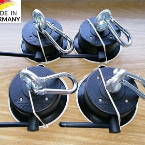 May include: Four black suction cup mounts with a silver swiveling hook and a lever to lock the hook in place. Each mount has a white ring around the base. The text "MADE IN GERMANY" is visible in the top left corner of the image.