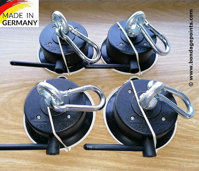May include: Four black suction cup mounts with a silver swiveling hook and a lever to lock the hook in place. Each mount has a white ring around the base. The text "MADE IN GERMANY" is visible in the top left corner of the image.