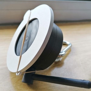 May include: White and black circular device with a rubber band wrapped around it. The device has a black antenna and a silver hook.