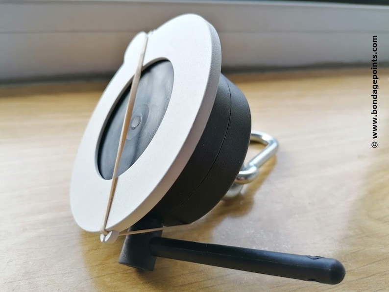 May include: White and black circular device with a rubber band wrapped around it. The device has a black antenna and a silver hook.