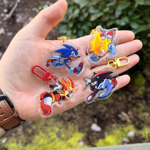 May include: A collection of clear acrylic keychains featuring various characters from the Sonic the Hedgehog video game series. The keychains showcase characters in action poses, with vibrant colors and attached metal clasps for easy attachment.