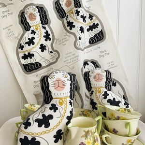 May include: A black and white fabric pattern for a dog cushion. The pattern includes instructions for sewing the cushion and the text "Front Dog One", "Back Dog One", "Stitch within the outer grey edge from A to B", "Pop me on the mantelpiece", and "Cut along the dotted line".