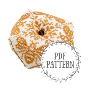 Könnte beinhalten: Ein sechseckiger Nadelkissen mit einem geometrischen Muster in Weiß und Senfgelb. Das Nadelkissen hat ein Loch in der Mitte für Nadeln.