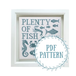 May include: A white frame containing a blue and white cross-stitch design that reads "Plenty of Fish". The design includes various sea creatures, such as fish, a crab, and a seahorse. A blue circle with white text reads "PDF Pattern".