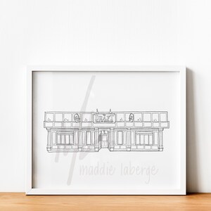May include: Black and white line drawing of a building in a white frame. The building has a sign that says "DRAFT Bar & Grille". The artist's name, "maddie laberge", is written in cursive at the bottom of the frame.