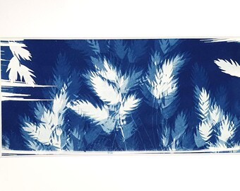 May include: A cyanotype print featuring a deep blue background with white silhouettes of wheat stalks and grasses. The rectangular artwork is centered within a wide, plain white mat board, creating a high-contrast botanical composition.