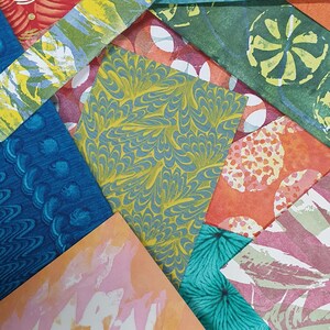 May include: A collection of overlapping rectangular paper sheets featuring diverse patterns and colors, including marbled yellow and blue, teal floral prints, orange circles, pink abstract washes, and architectural gray line designs.