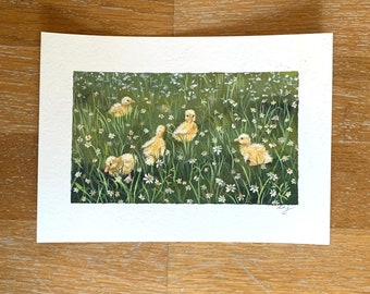 May include: An original watercolor painting of six yellow ducklings in a field of green grass and white daisies. The artwork is on white paper and signed in the lower right corner. The painting has a soft, natural aesthetic.