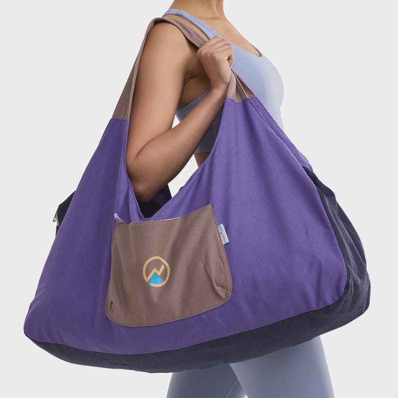 May include: A large, purple tote bag with a brown pocket and a mountain logo. The bag has a black base and brown straps. The bag is made of a soft material and is designed to be carried over the shoulder.