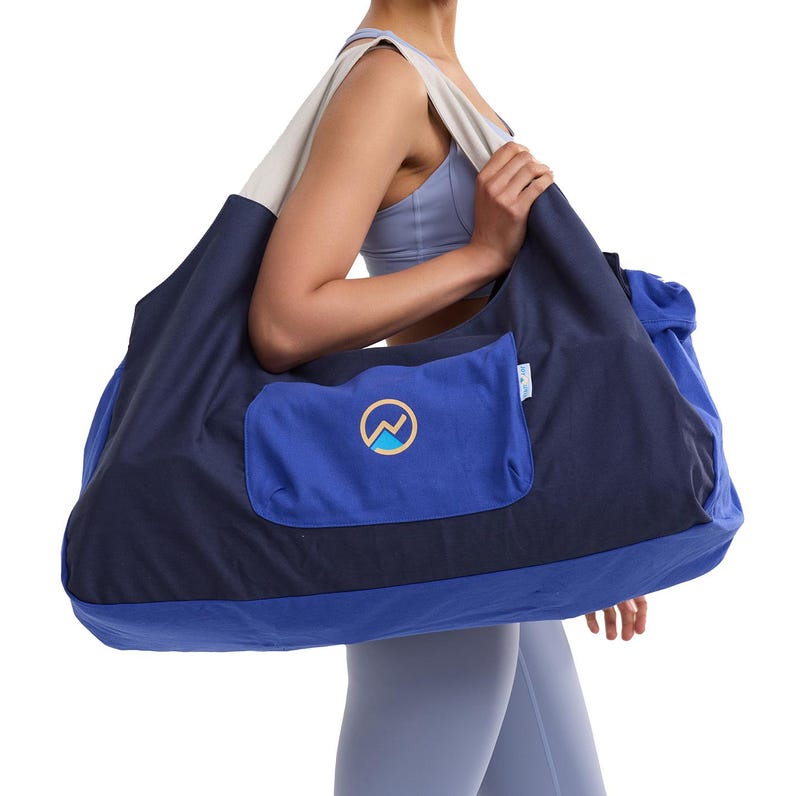 May include: A large navy blue and light blue tote bag with a light beige strap. The bag has a front pocket with a logo. The bag is designed for carrying items. The bag is made of a durable fabric.
