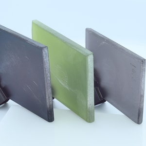 Puede incluir: Tres paneles de vidrio rectangulares, uno verde, uno gris oscuro y uno gris claro, se muestran sobre una superficie blanca. Los paneles están ligeramente esmerilados y tienen una textura sutil.