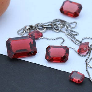 May include: A silver chain necklace with five red gemstone pendants. The gemstones are cut into rectangular shapes with beveled edges.