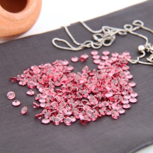 May include: A close-up of a pile of pink gemstones on a black fabric surface. A silver chain necklace is visible in the background.