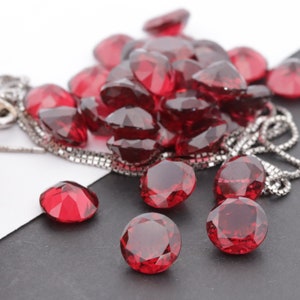 Puede incluir: Un montón de cuentas de piedras preciosas rojas, algunas de las cuales están enhebradas en una cadena de plata. Las cuentas son redondas y tienen un corte facetado.