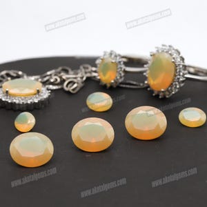 May include: An assortment of opal gemstones and jewelry. The image features oval-shaped opals in various sizes, along with two rings and a pendant necklace. The opals have a milky, iridescent appearance, with a mix of yellow and white hues.