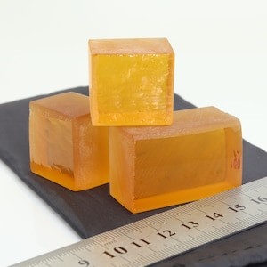 May include: Three clear amber rectangular blocks stacked on top of each other on a black surface. A silver ruler with black markings is in the foreground.