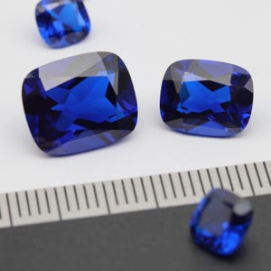 May include: Four blue gemstone cushion cut loose stones of varying sizes. The stones are faceted and have a high level of brilliance.