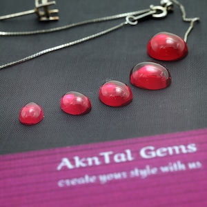 May include: Five red gemstones of varying sizes are arranged in a row on a black surface. The gemstones are round and have a smooth, polished finish. The text "AknTal Gems create your style with us" is visible in the background.