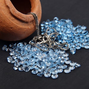 May include: A clay pot with a silver chain pouring out a large pile of light blue gemstones on a black surface.
