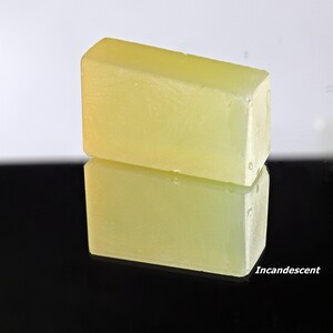 Puede incluir: Dos barras rectangulares de jab&oacute;n amarillo p&aacute;lido, una apilada sobre la otra, reflej&aacute;ndose en una superficie negra.