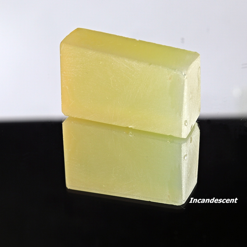 Puede incluir: Dos barras rectangulares de jab&oacute;n amarillo p&aacute;lido, una apilada sobre la otra, reflej&aacute;ndose en una superficie negra.
