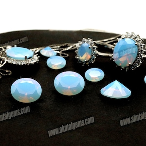 May include: A collection of opalescent gemstones and jewelry pieces. The gemstones are oval and faceted, displaying a soft blue and white color. Several pieces of jewelry, including rings and pendants, are also visible, featuring similar opalescent stones.