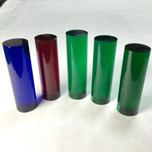 Op de afbeelding: Vijf cilindrische objecten in blauw, rood en groen. Elke cilinder heeft een donkere basis en bovenkant, met een doorschijnend lichaam. De objecten zijn verticaal gerangschikt en tonen hun kleurvariaties.