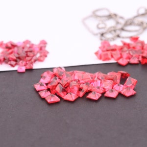 Puede incluir: Un montón de pequeñas piedras preciosas cuadradas de color rosa sobre una superficie negra. Las piedras preciosas están dispersas y algunas se superponen.