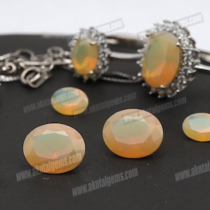 May include: A collection of opalescent gemstones and two silver rings featuring oval opals. The gemstones are in different sizes and shapes, including round and oval cuts. The opals display a milky, iridescent appearance.