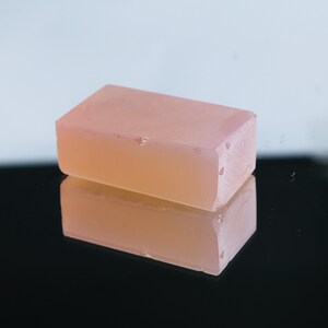Puede incluir: Una barra rectangular de jab&oacute;n rosa transl&uacute;cido con una superficie ligeramente texturizada.