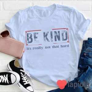 Puede incluir: Una camiseta azul claro con el texto "BE KIND it's really not that hard" en una fuente azul desgastada. El texto est&aacute; encerrado en un rect&aacute;ngulo rojo.