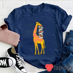 以下が含まれることがあります： 青いTシャツに、眼鏡をかけ、カラフルな本を積み重ねている黄色のキリンのグラフィックがプリントされています。